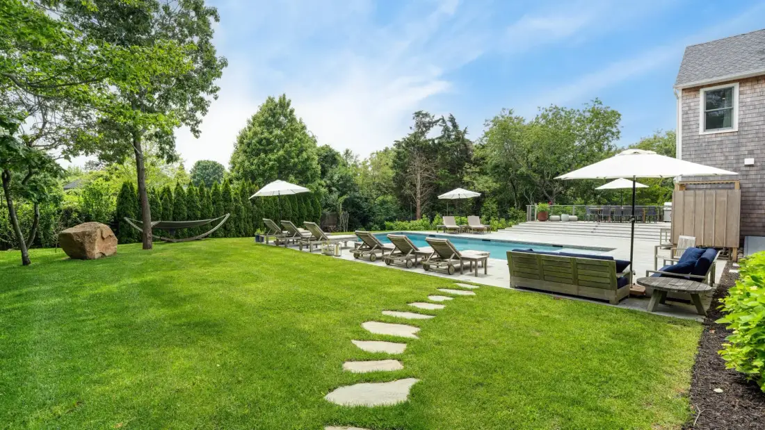 Un patio ajardinado con césped, piedras de paso y una zona de descanso junto a la piscina.