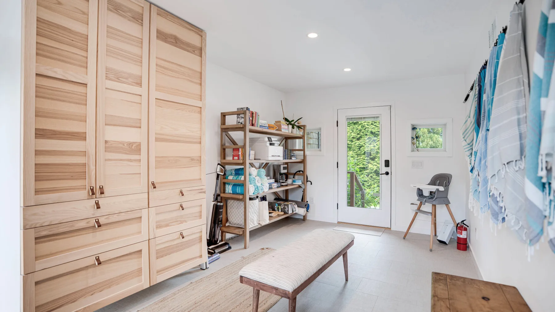 Una habitación luminosa con armarios de madera, estanterías abiertas y un banco acolchado.