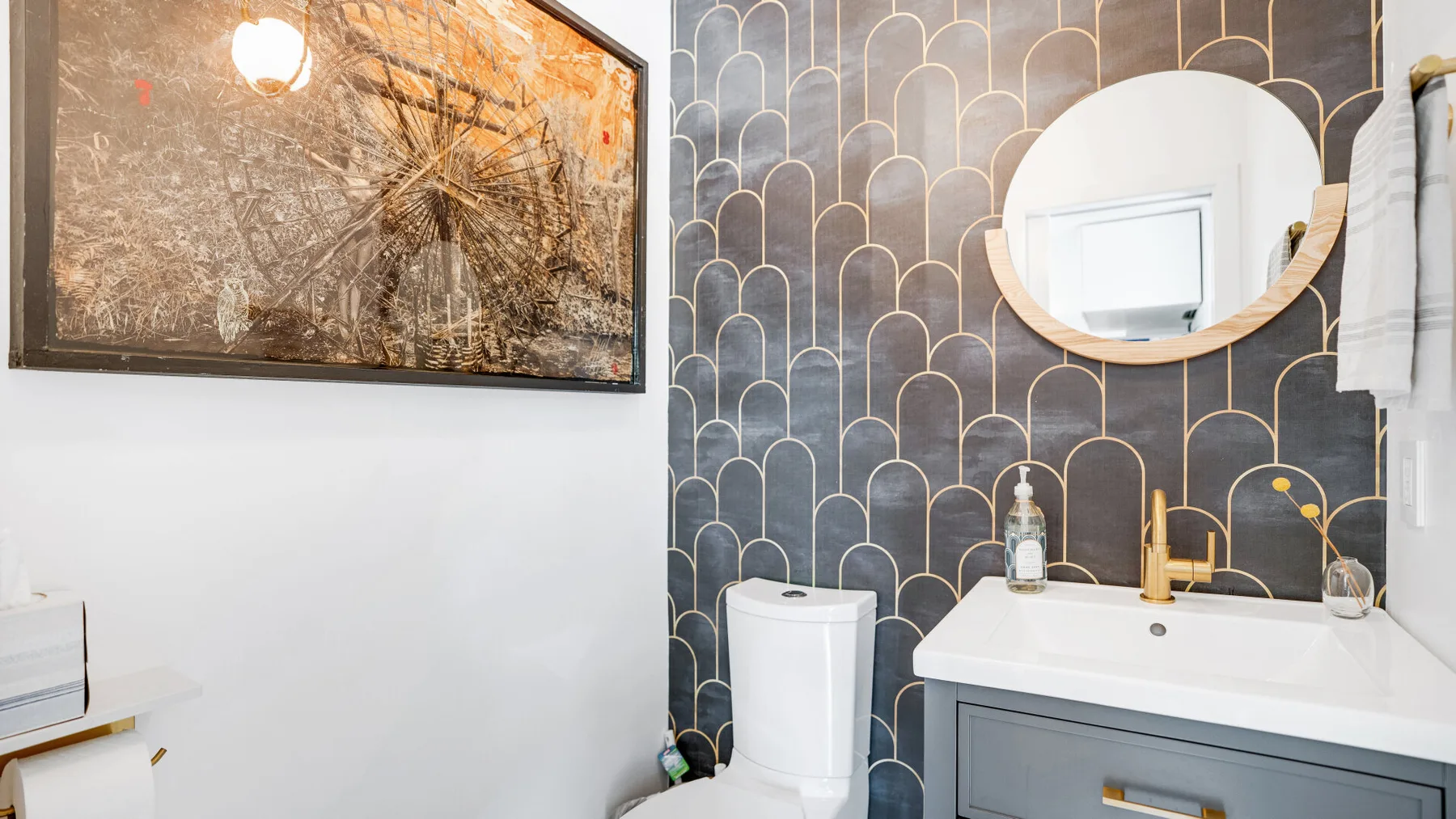 Un baño con mueble de lavabo, lavabo, inodoro y una pared oscura estampada.