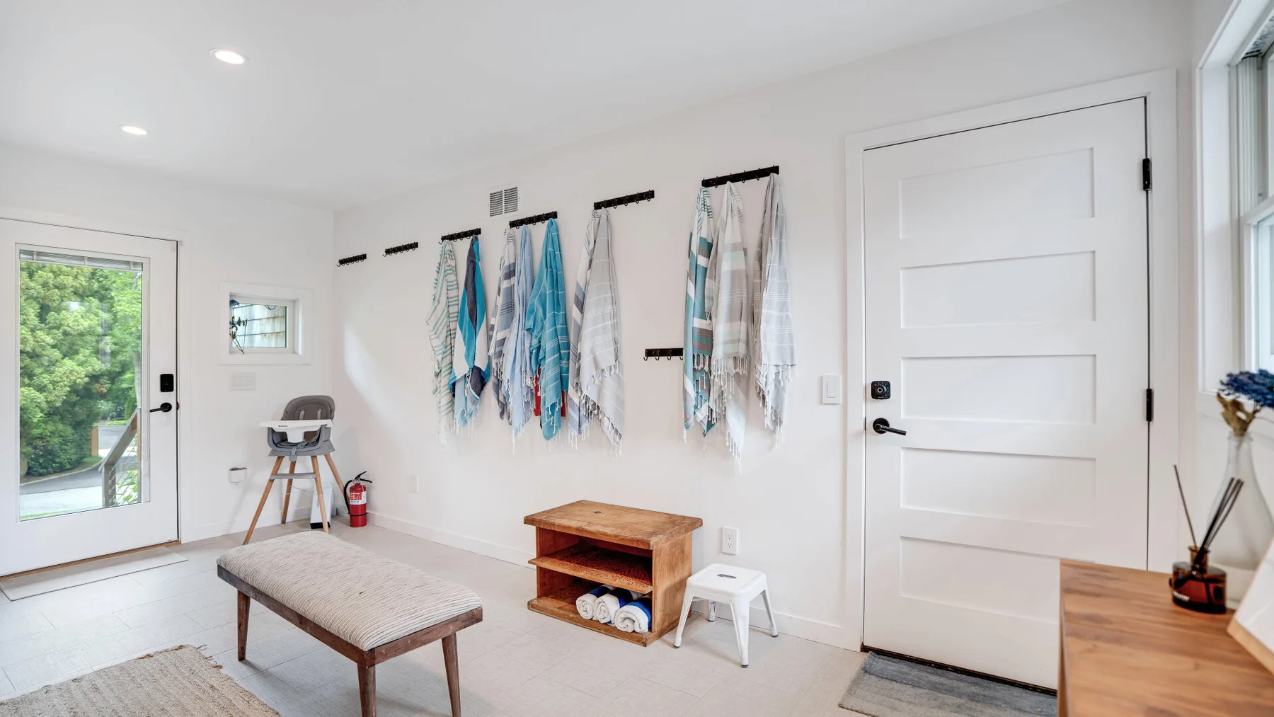 Una habitación luminosa con un banco acolchado, ganchos en la pared y una puerta cerrada.