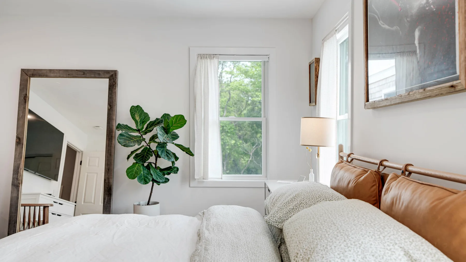 Un dormitorio luminoso con una cama, una planta frondosa y una ventana.