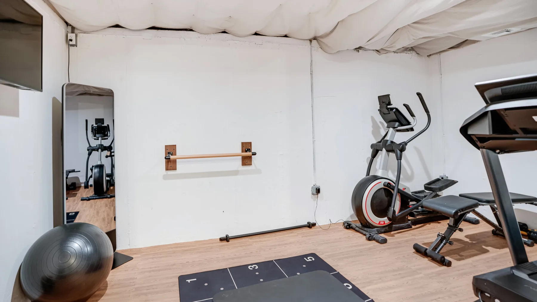 Una pequeña sala de ejercicio con máquinas cardiovasculares, un espejo y una esterilla.