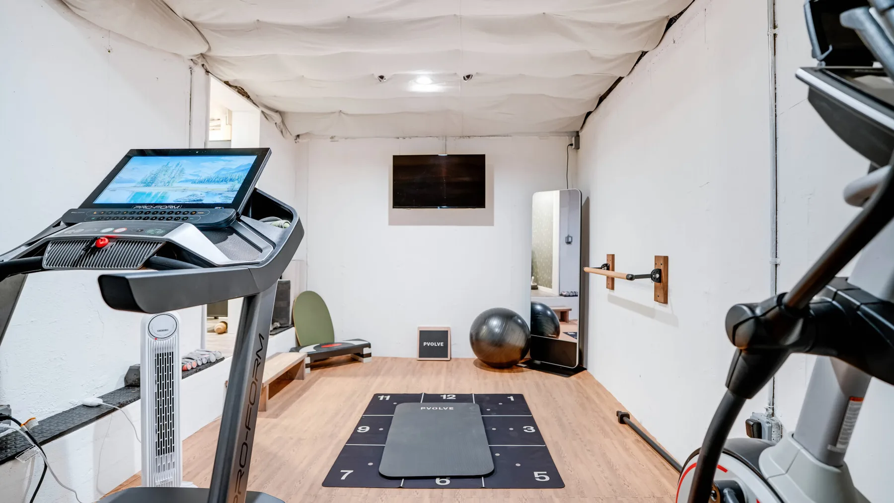 Una pequeña sala de ejercicio con cintas de correr y una colchoneta.