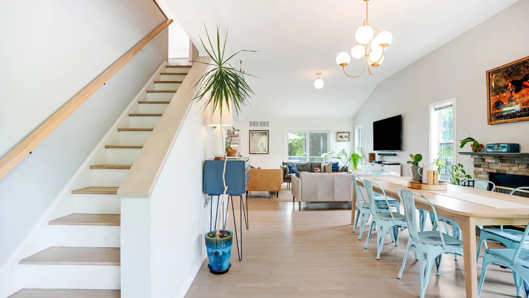 Un luminoso salón-comedor de planta abierta con una escalera y grandes ventanales.