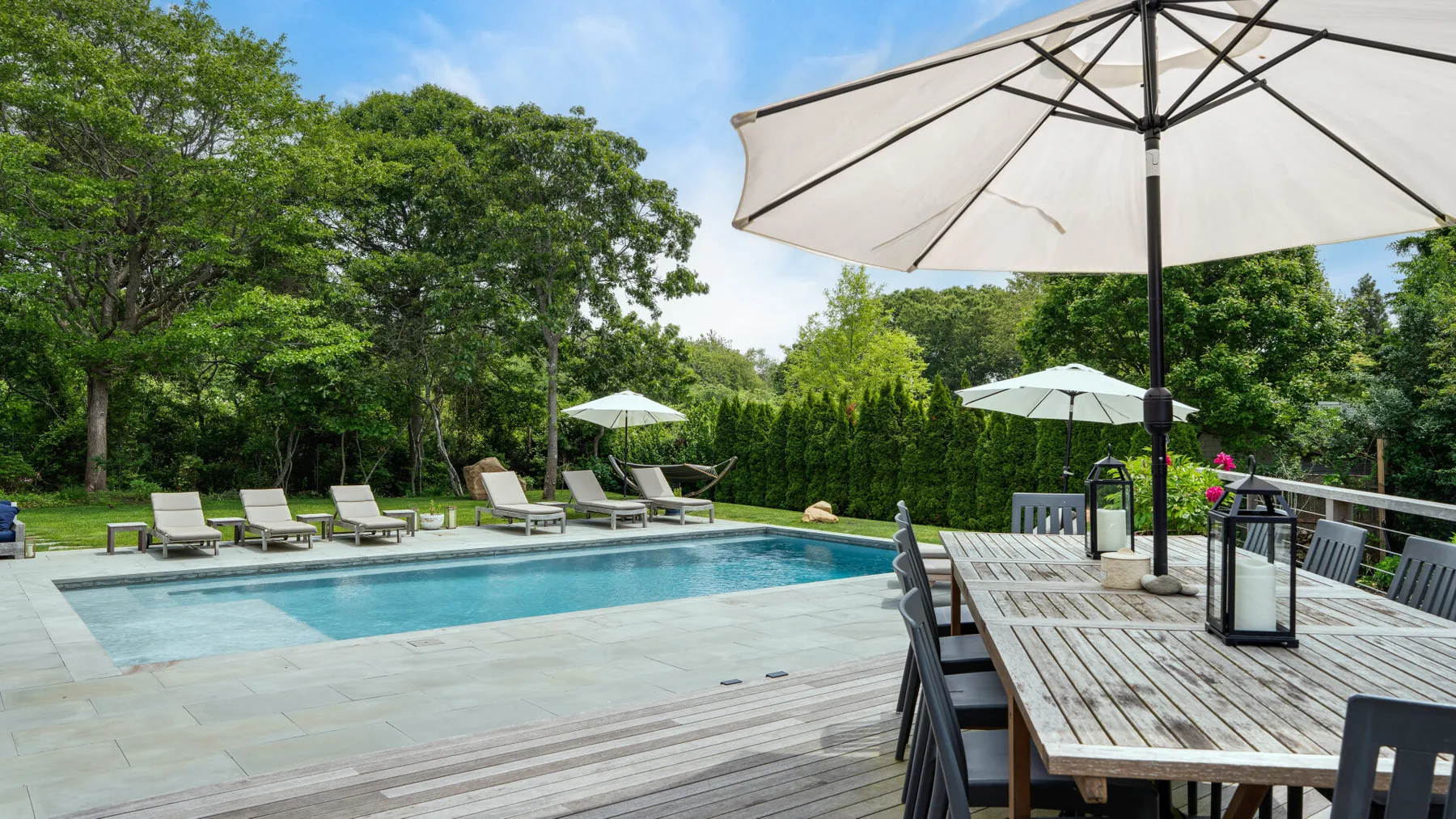 Una piscina al aire libre junto a una terraza de madera con mesas y sombrillas.