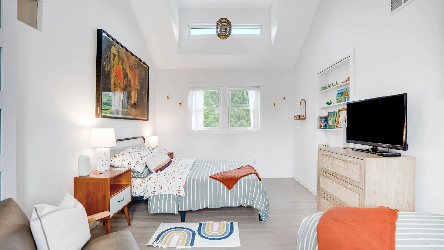 Un dormitorio luminoso con una cama a rayas, una mesita de noche y un televisor.