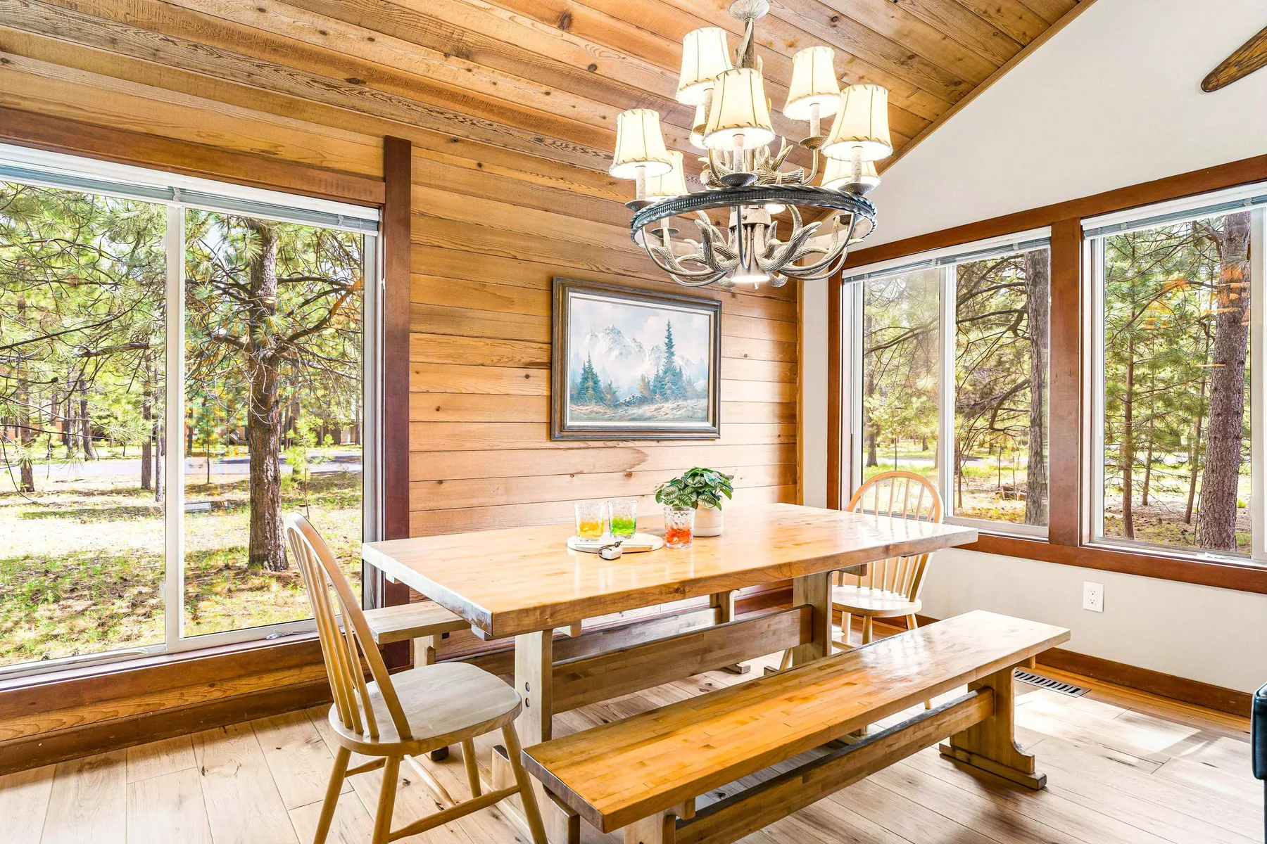 Comedor con paneles de madera, una mesa y grandes ventanas con vista a los árboles.