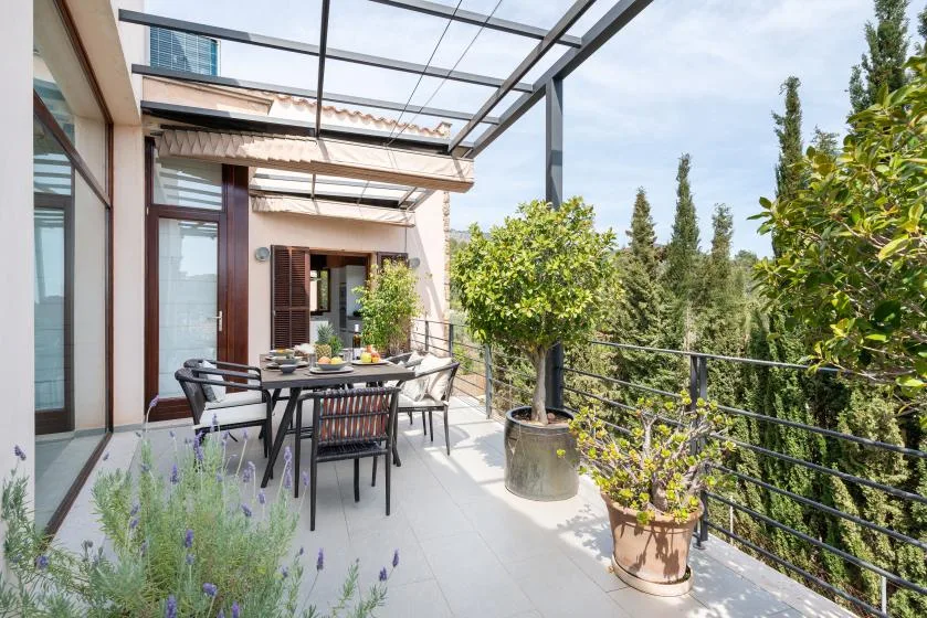 A covered outdoor dining terrace with a table, seating, and potted plants.