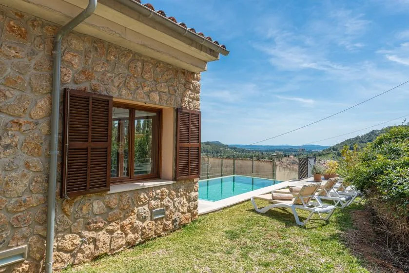 A stone house beside an outdoor swimming pool with lounge seating and distant hills.