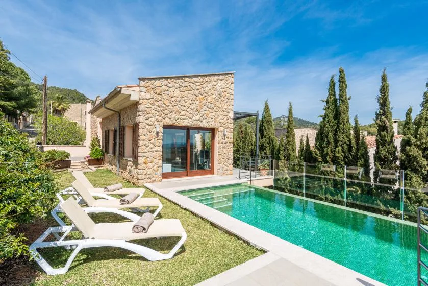 A pool beside a stone building, with lounge seating on the surrounding lawn.