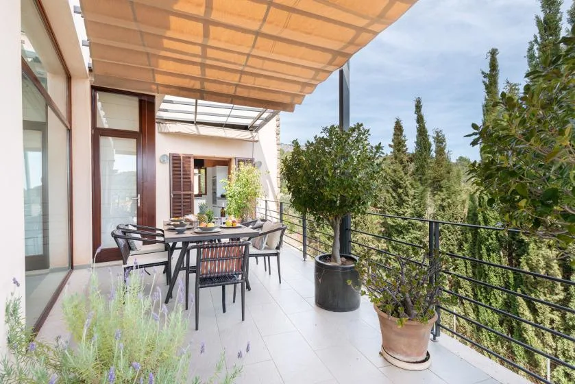 A covered patio with outdoor seating and potted plants beside a railing.