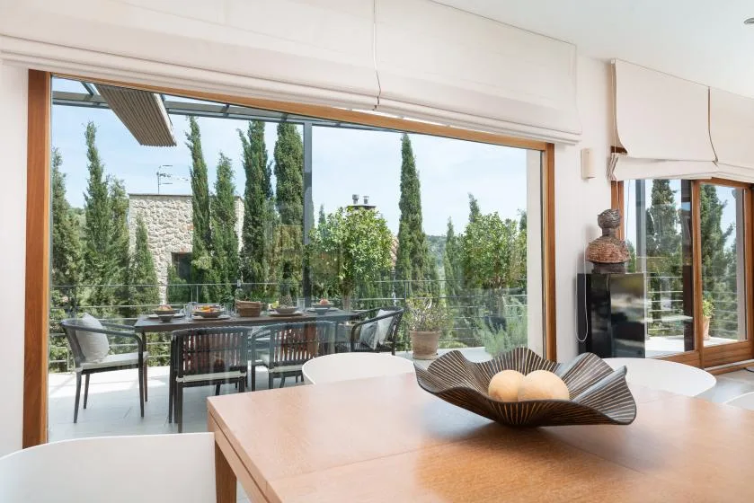 A bright dining area opens onto an outdoor patio with a table and greenery.