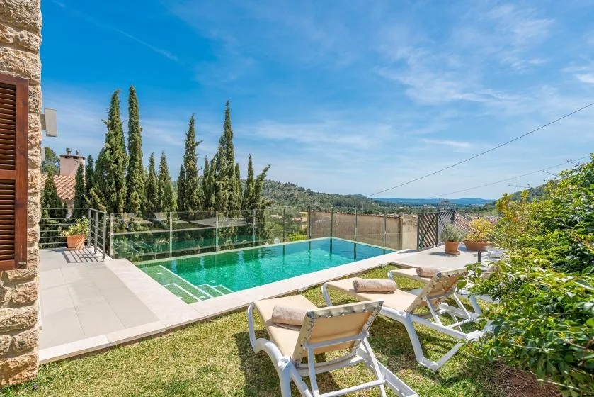 An outdoor swimming pool with lounge seating overlooks a green, hilly landscape.