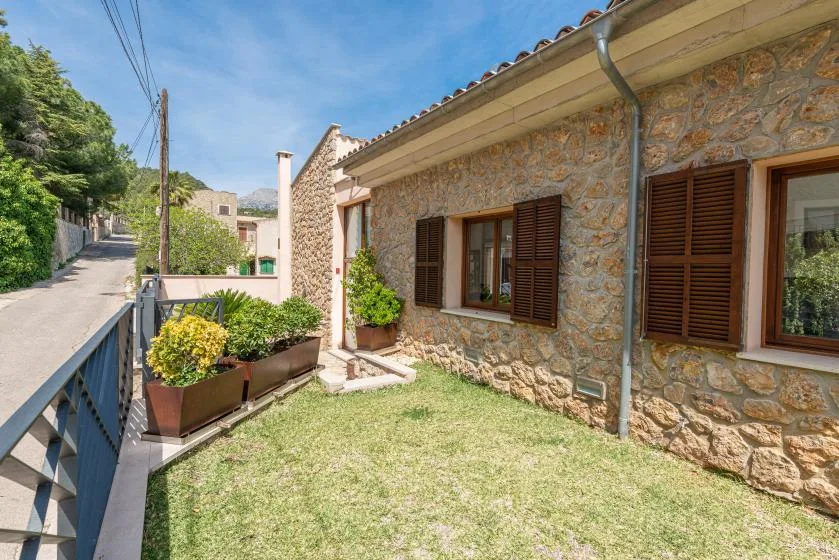 A stone house exterior with shuttered windows and a small grassy yard.
