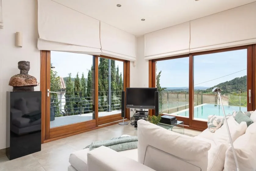 A bright living room with large windows overlooking a pool and green hills.