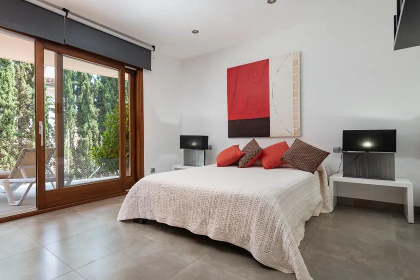 A bedroom with a bed beneath abstract wall art and large glass doors.