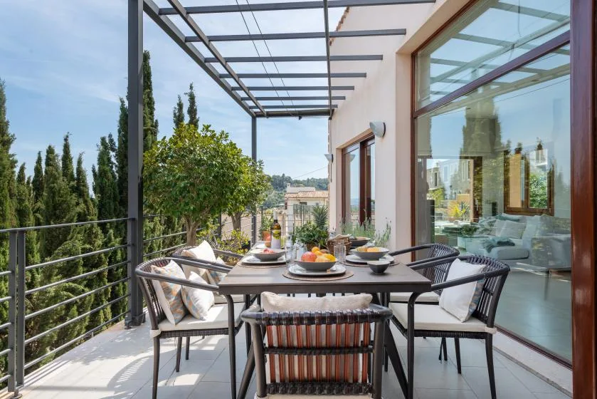 An outdoor dining table sits on a terrace beside large glass doors.