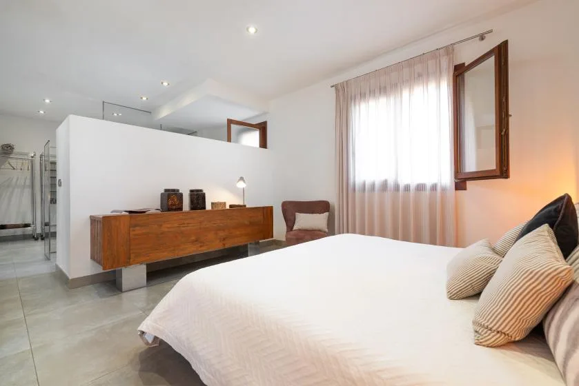 A bedroom with a large bed, wooden dresser, and a curtained window.