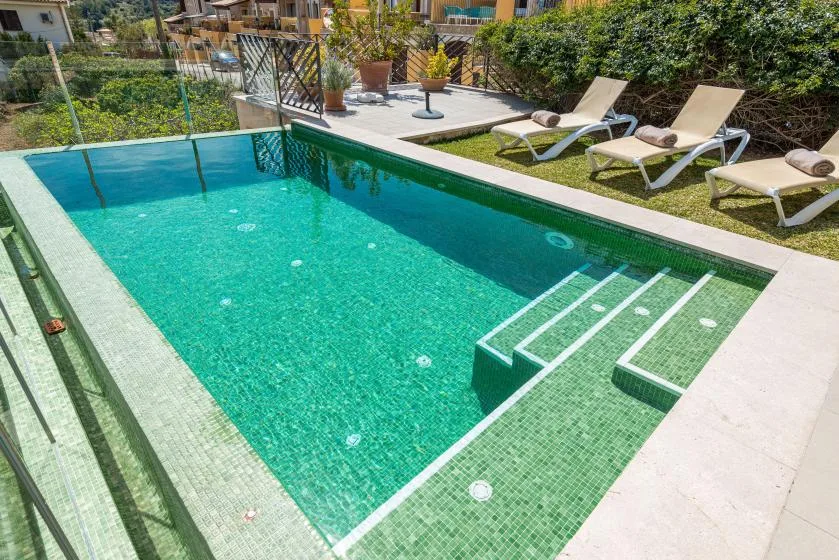 A turquoise swimming pool with submerged steps beside a small sunbathing area.