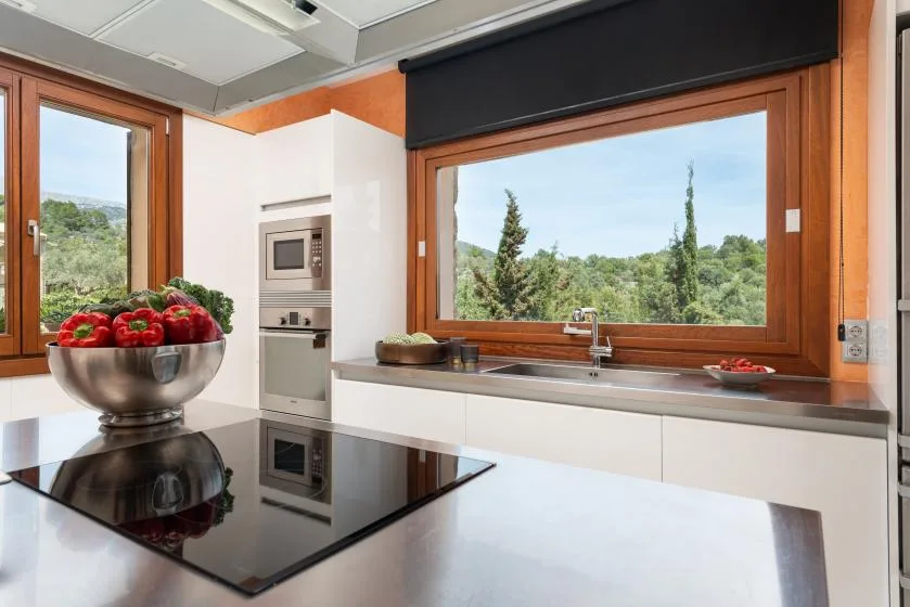 A modern kitchen with a wide window overlooking green trees.