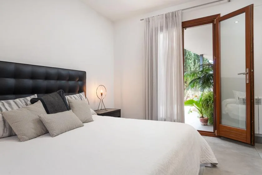 A bright bedroom with a large bed and an open glass door to greenery.