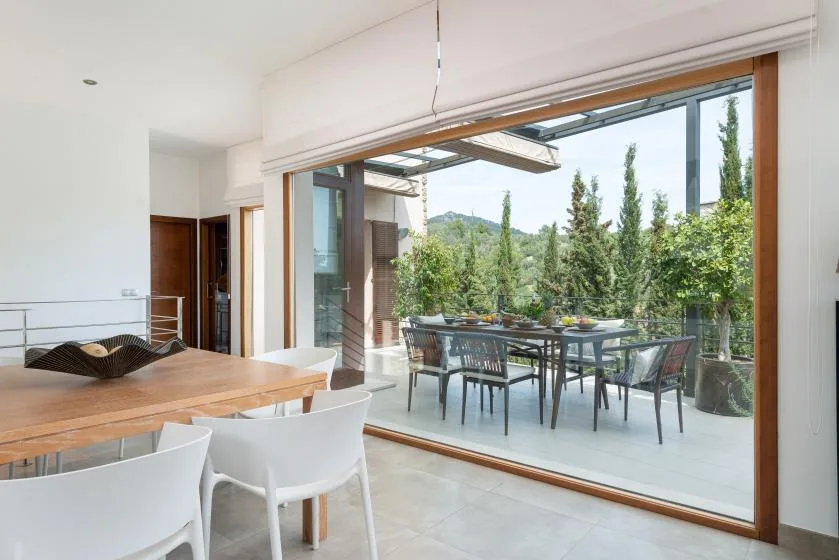 A dining area opens onto an outdoor terrace with a table and greenery.