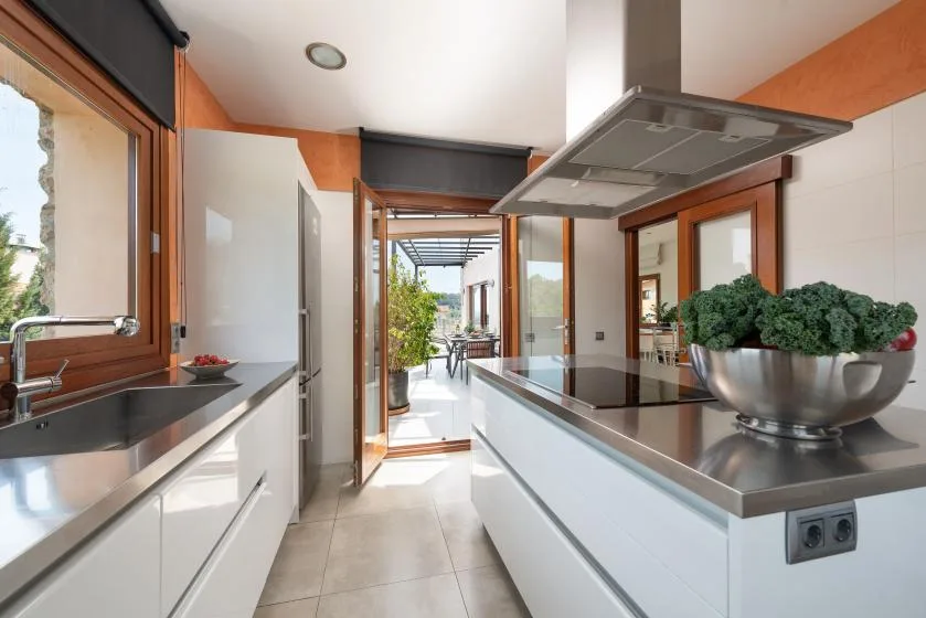 A modern kitchen with white cabinets, dark counters, and an open view to a patio.