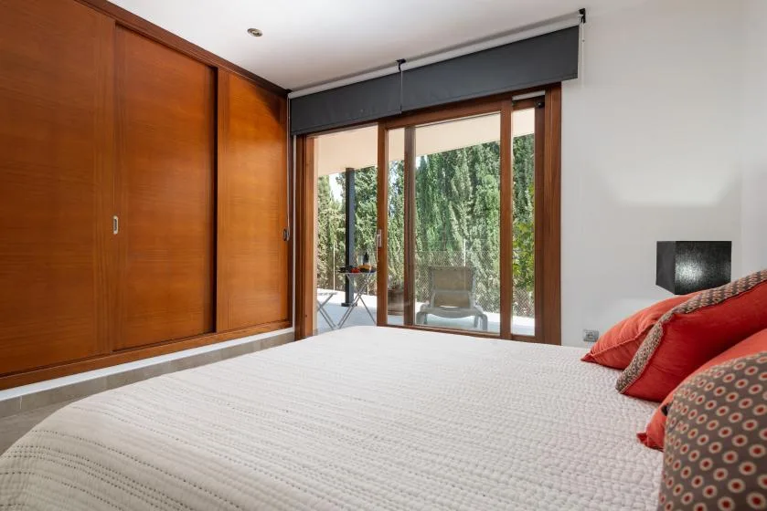 A bedroom with a large bed beside wooden closets and glass doors.
