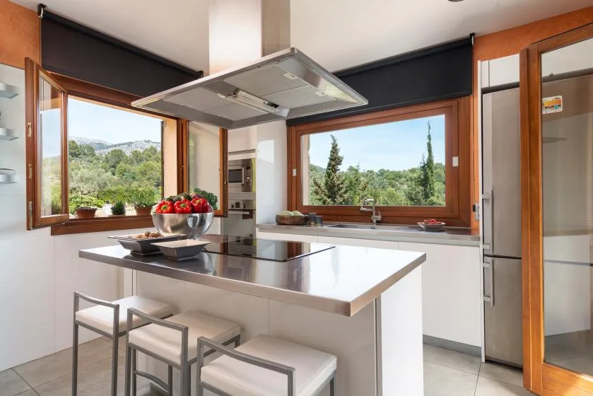 A bright kitchen with a central island and large windows overlooking greenery.