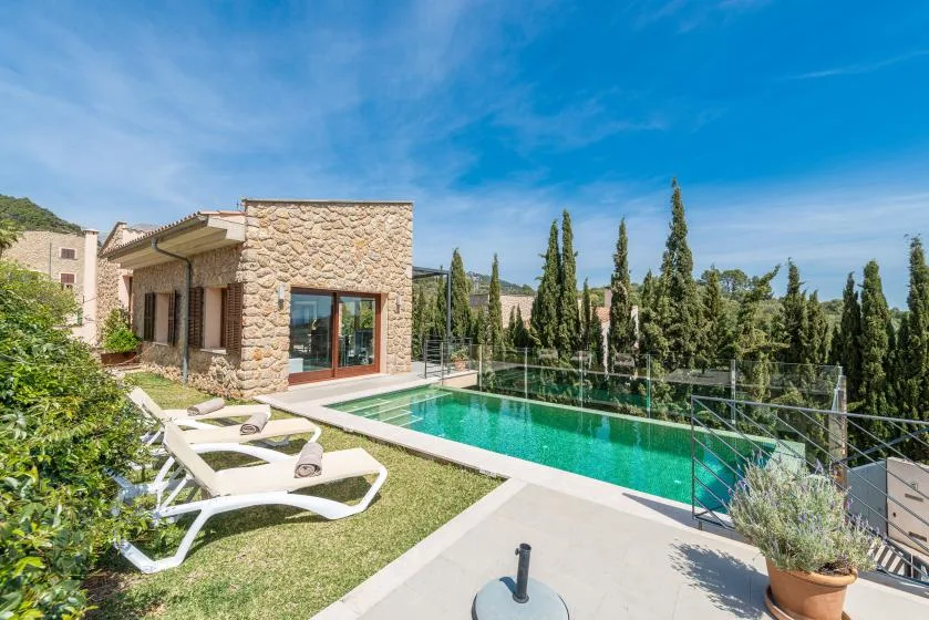 A stone house beside a swimming pool, with lounge chairs on the lawn.