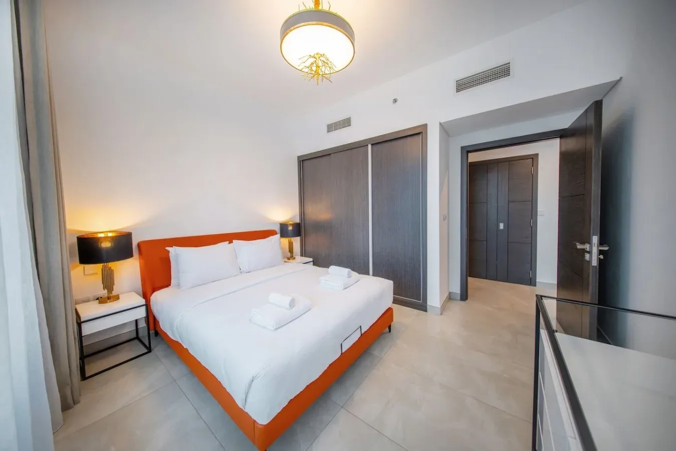 A bedroom with a white bed, orange bed frame, and bedside lamps.