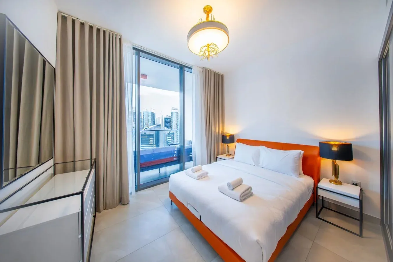 A bedroom with a white bed, bedside lamps, and a glass door opening to a balcony.