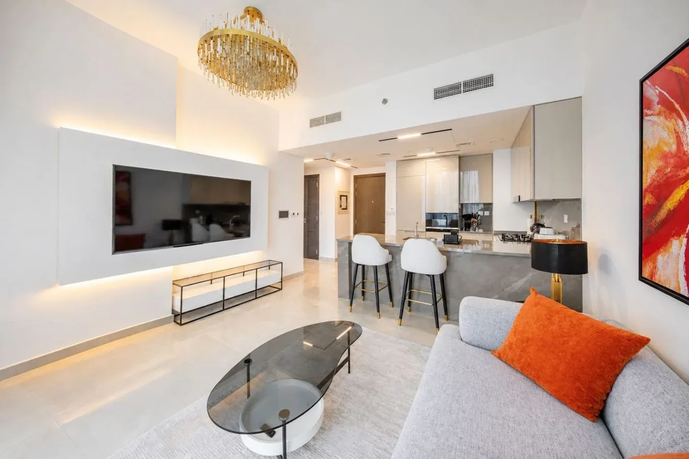 A bright living room opens onto a kitchen, with a wall-mounted television and seating.