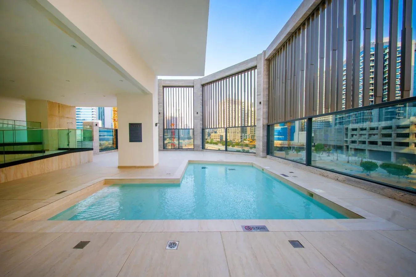 A rooftop swimming pool sits beside tall windows overlooking nearby buildings.