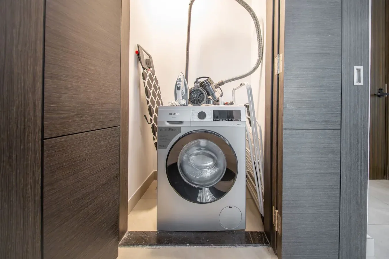 A compact laundry area with a front-loading washing machine and ironing board.
