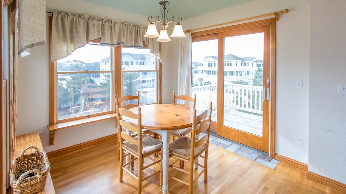 A dining area with a wooden table and chairs beside large windows and a glass door.