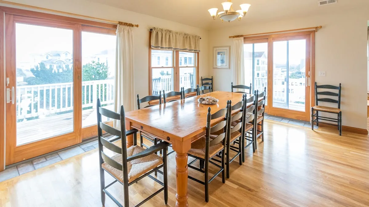 A dining room with a wooden table and large windows.