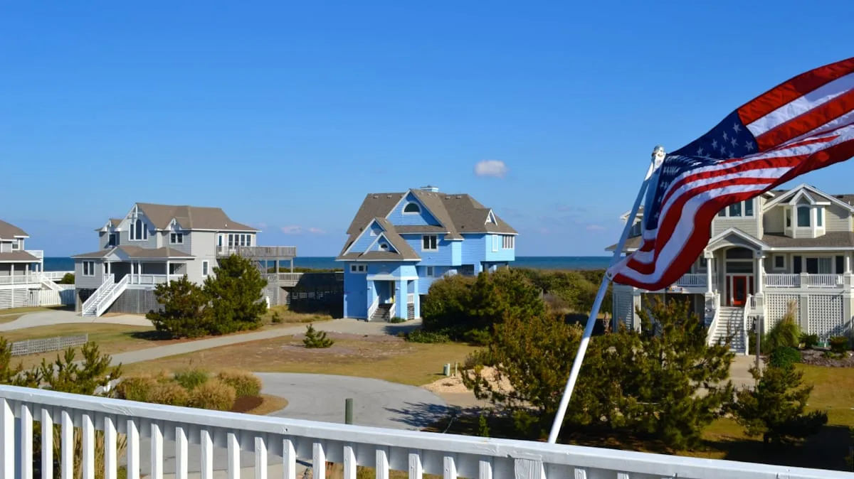 Coastal homes stand beside a road, with an American flag in the foreground.