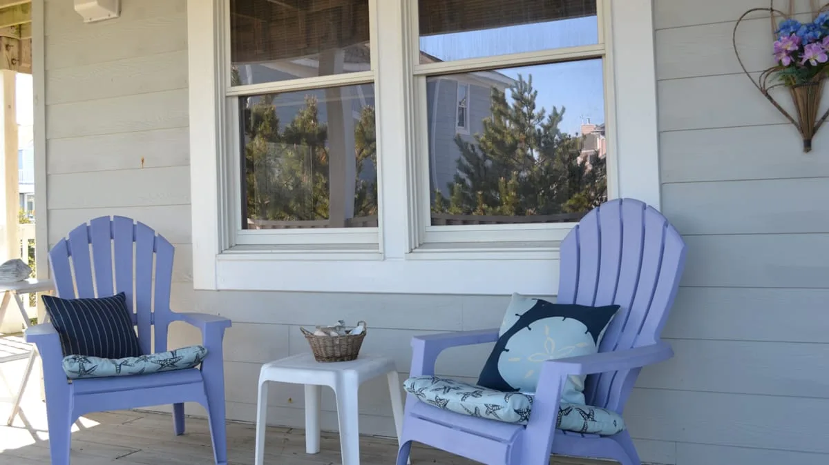 A porch seating area with two purple chairs beside large windows.