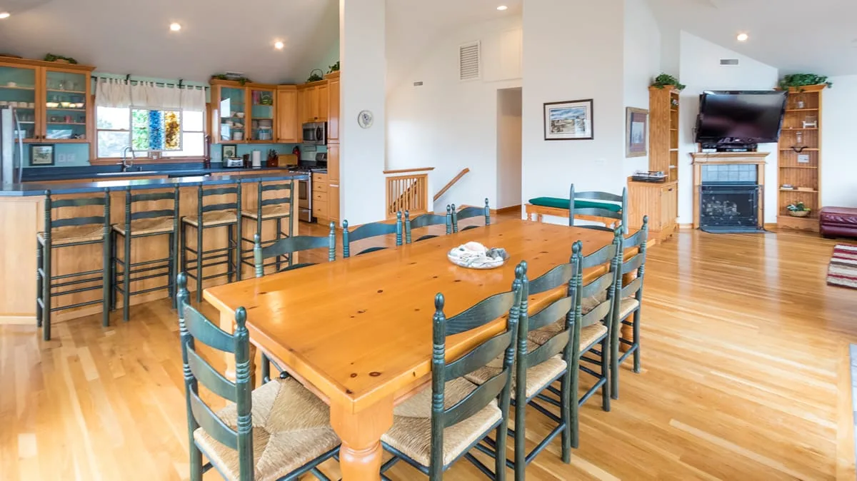 An open-plan dining and living area with a large wooden table and kitchen bar.