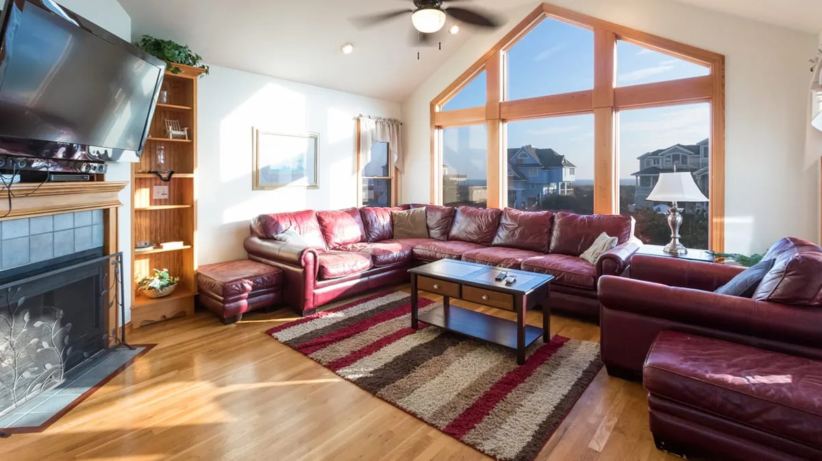 A bright living room features a large sectional seating area beside tall windows.