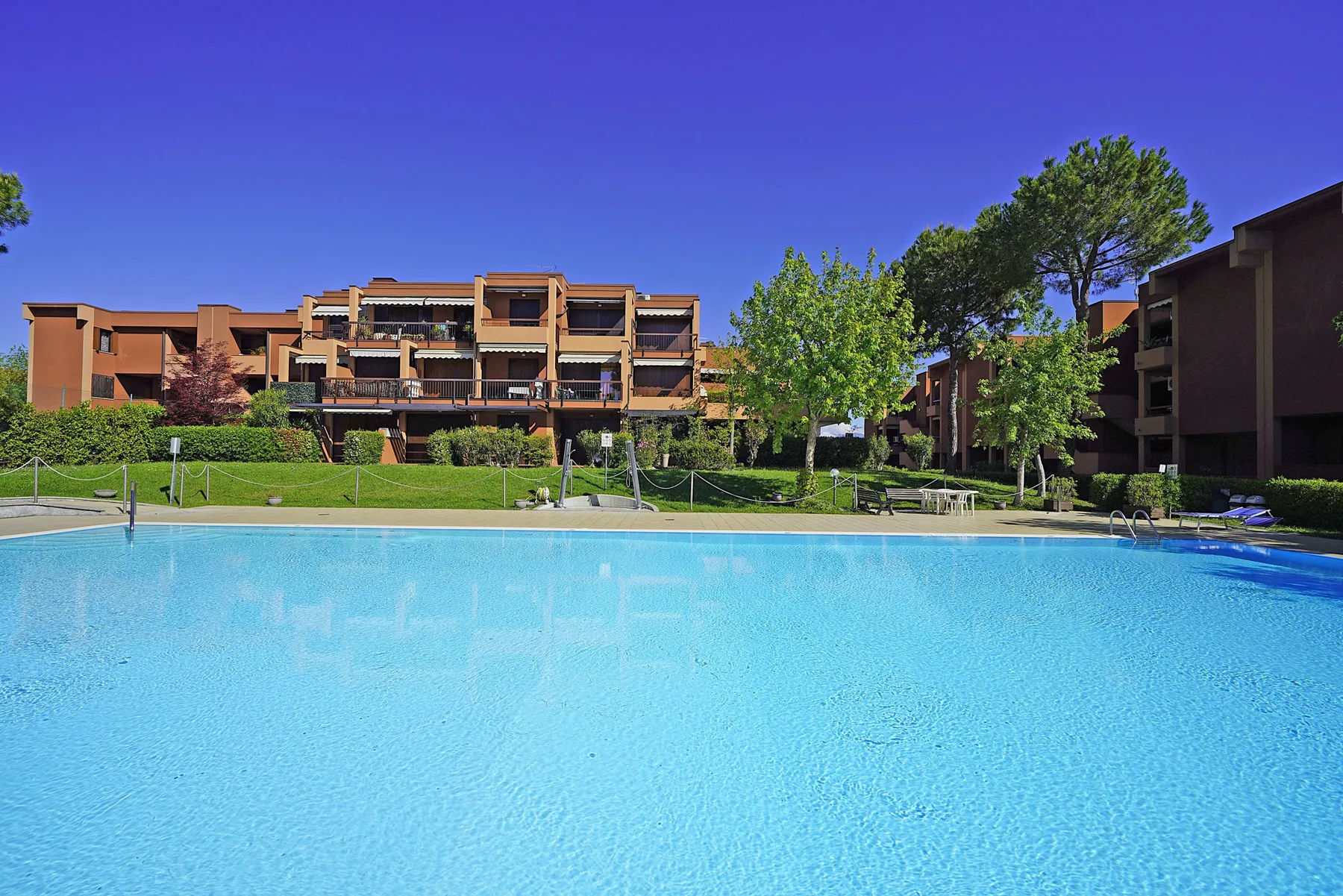 A swimming pool in front of apartment buildings, with trees along the far side.
