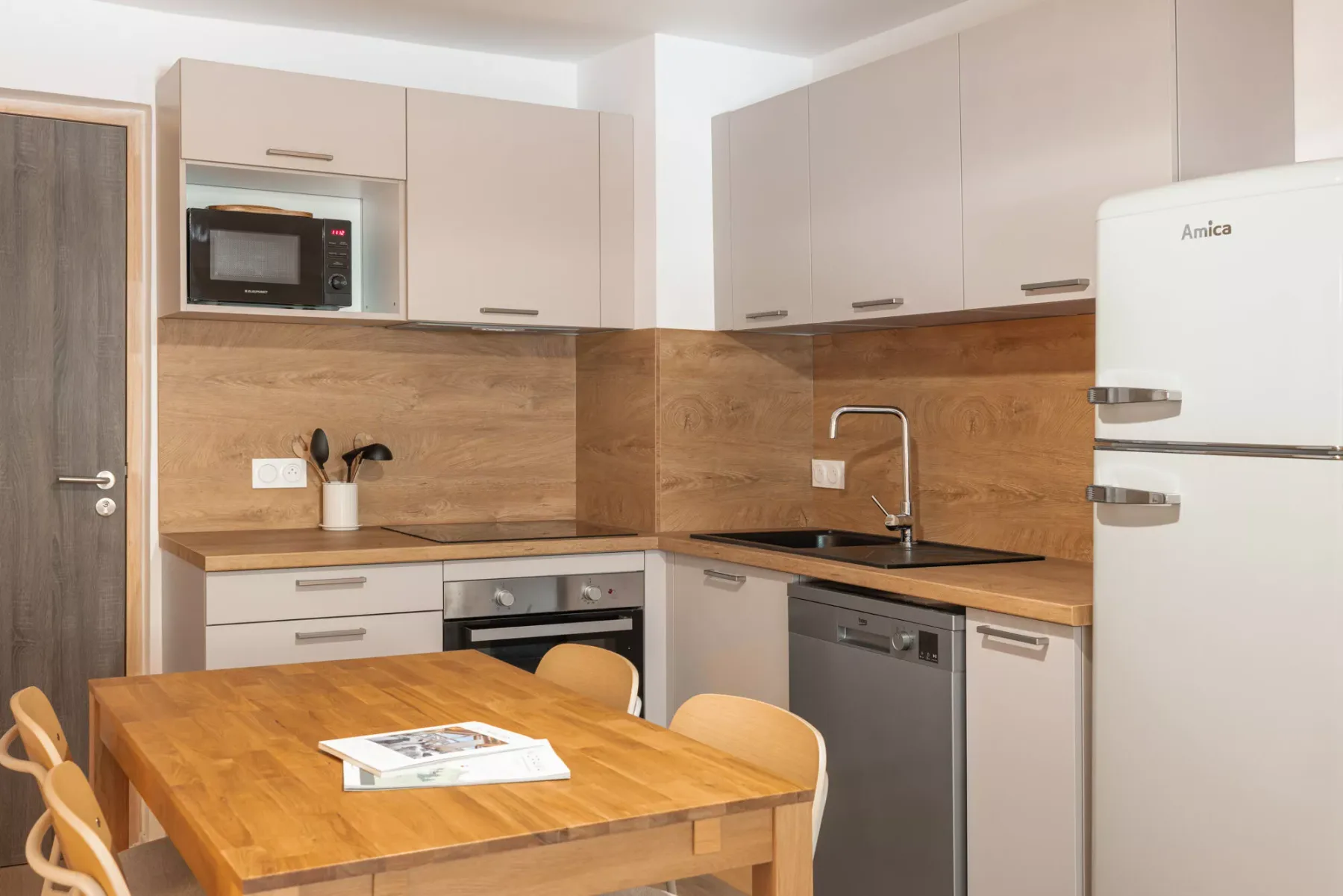 A kitchen with pale cabinets, a dark countertop, and a wooden dining table.