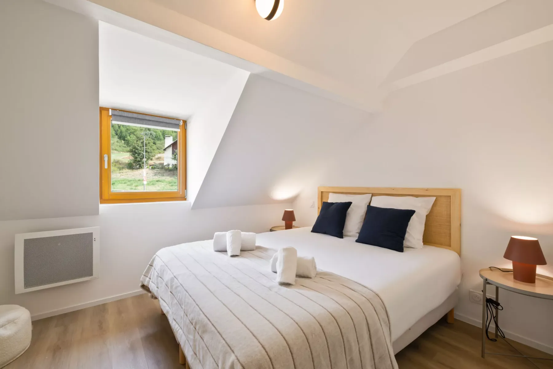 Un dormitorio luminoso con una cama bien tendida bajo un techo inclinado.