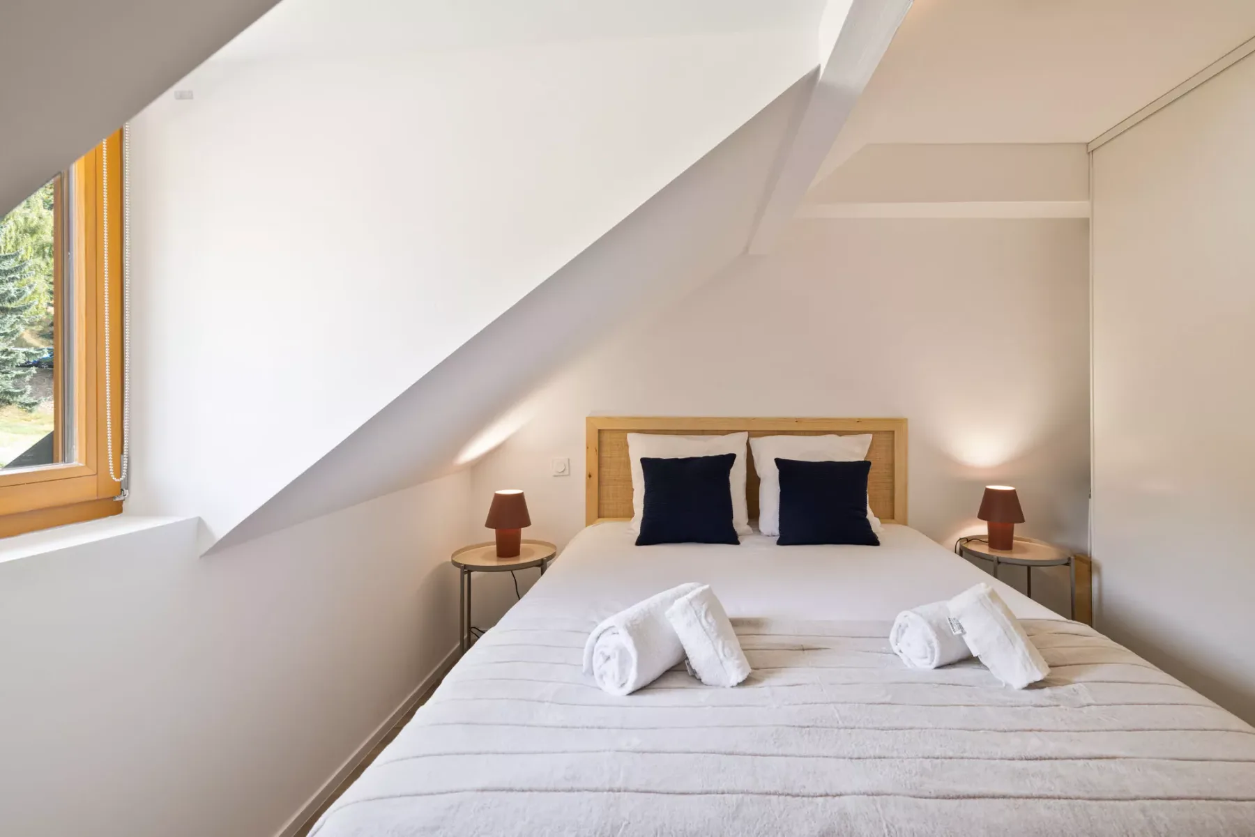 A bright attic bedroom with a bed beneath a sloping ceiling.