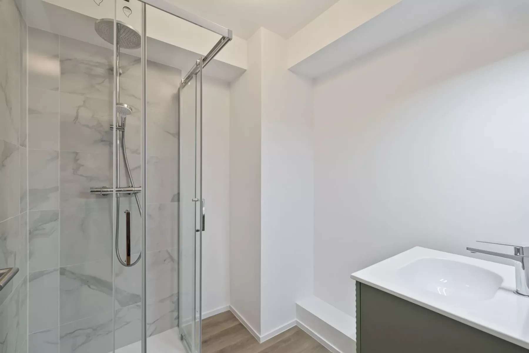 Un baño con ducha de vidrio y un lavabo blanco.