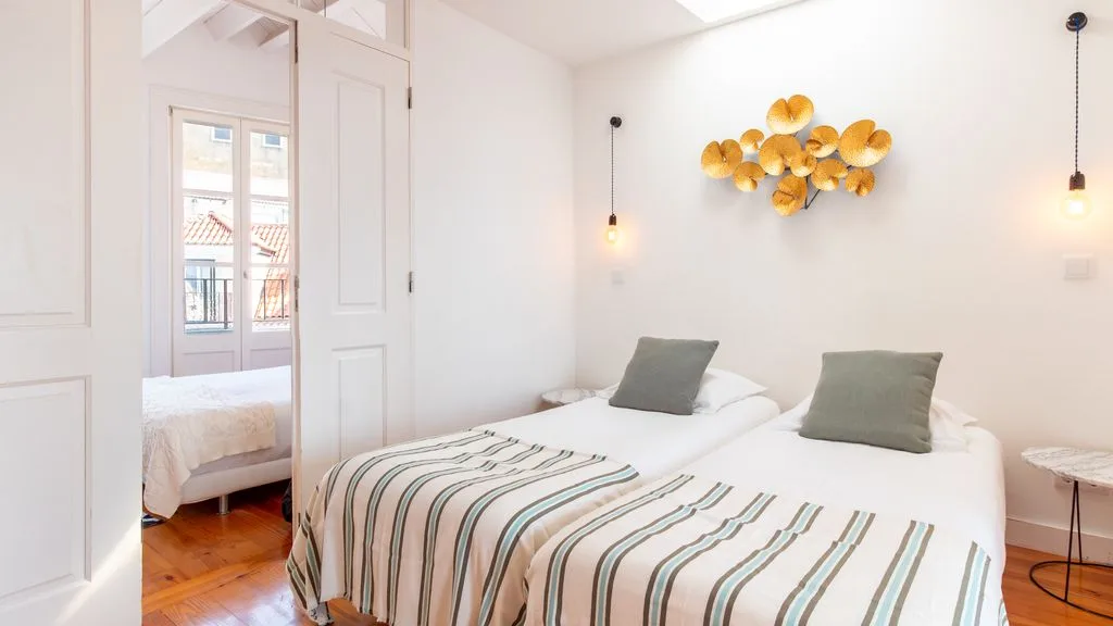 Un dormitorio luminoso con una cama, ropa de cama a rayas y decoración dorada en la pared.