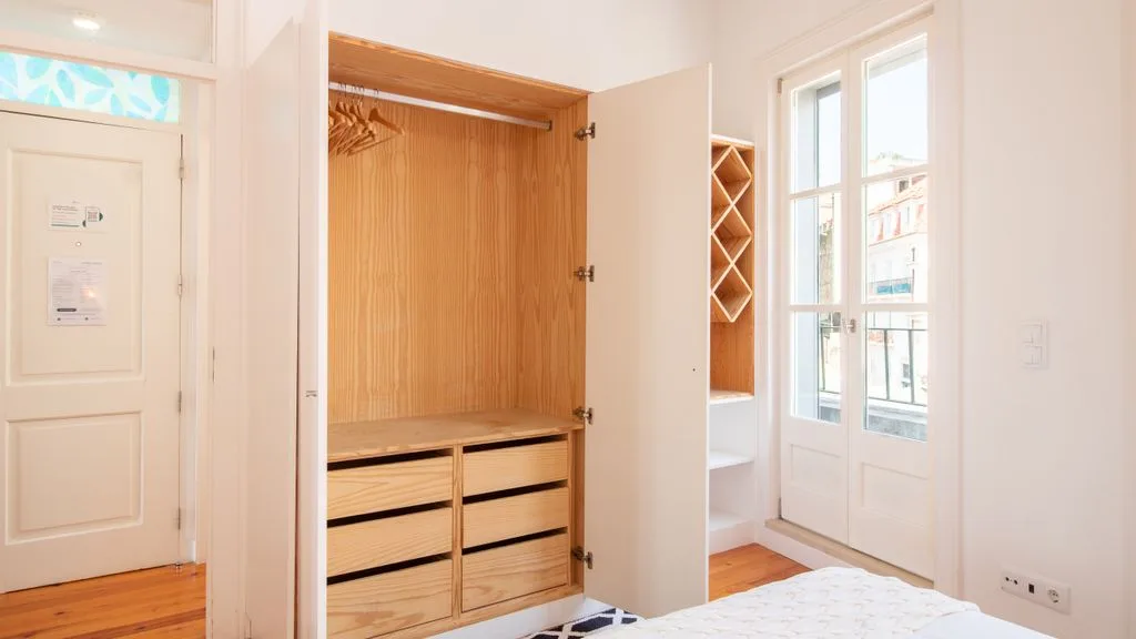 Un vestidor luminoso con un armario de madera abierto junto a una ventana.