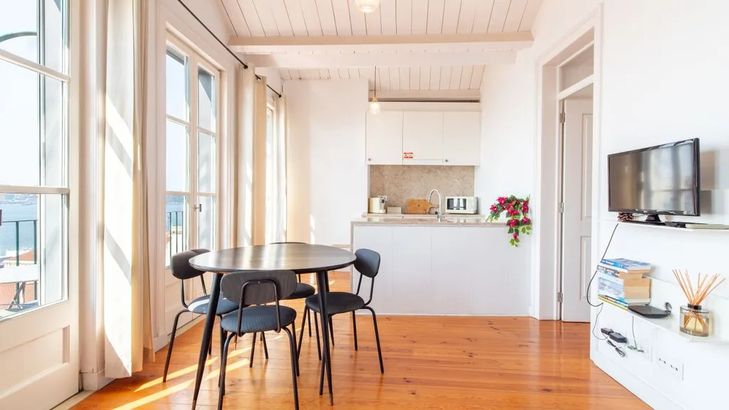 Una luminosa zona de comedor y estar con una mesa redonda junto a ventanas altas.