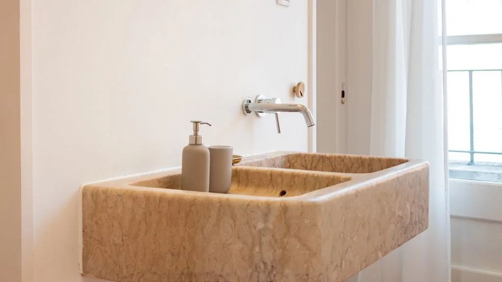Un lavabo de baño con grifo de pared junto a una ventana luminosa.